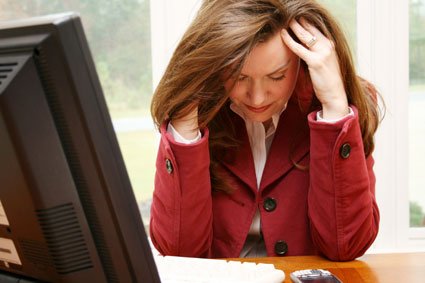 Woman with head in her hands at a computer desk.